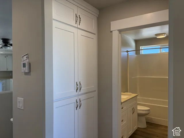 Full-height white built-in cabinetry with brushed metal hardware, white vanity with integrated basin, tub and shower combination with surround, and wood-finish flooring