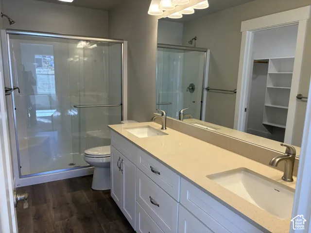 Dual-sink vanity with light-toned solid surface countertops, wood-finish flooring, glass-enclosed shower, and walk-in closet with built-in shelving