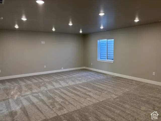 Neutral-toned interior space featuring recessed ceiling lighting, wall-to-wall carpeting, and a single window with an egress-style exterior well