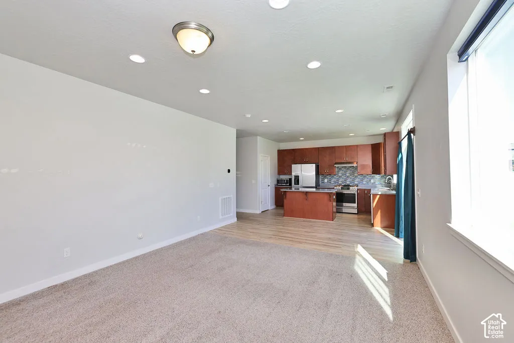 Open-concept interior featuring recessed lighting, wood-finish flooring in the kitchen area, carpeted flooring in the living area, wood-finish cabinetry, and a kitchen island