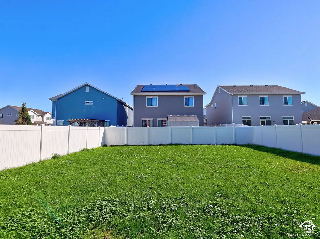 Fenced backyard featuring an expansive lawn area and multi-story residence with rooftop solar panels