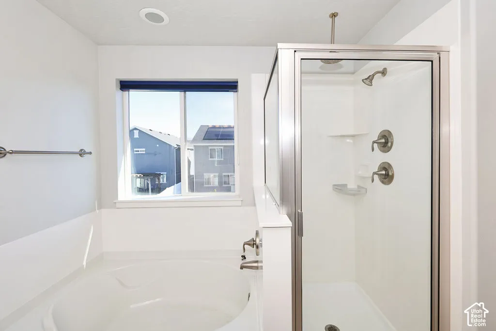 Soaking tub with a wall-mounted faucet, separate enclosed shower stall, recessed ceiling lighting, and a window with natural light