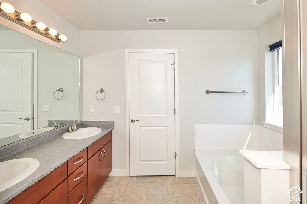 Double-sink vanity with stone-finish countertop, full-width vanity mirror, five-light fixture, and built-in soaking tub
