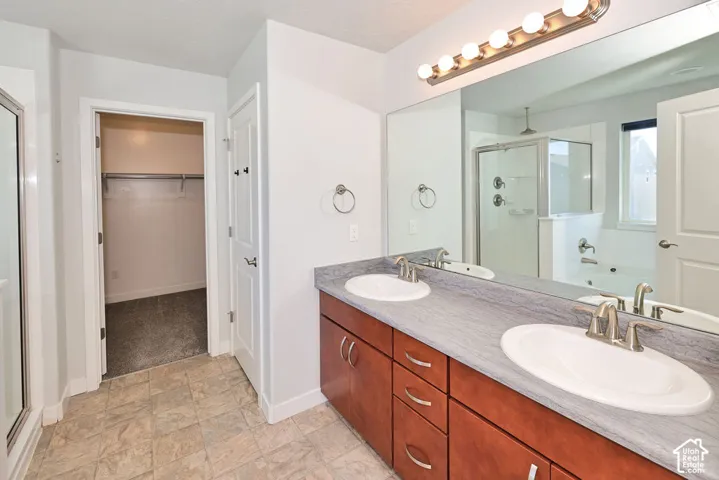 Dual-sink vanity with wood-finish cabinetry, countertop with integrated backsplash, expansive wall-mounted mirror, and tile flooring