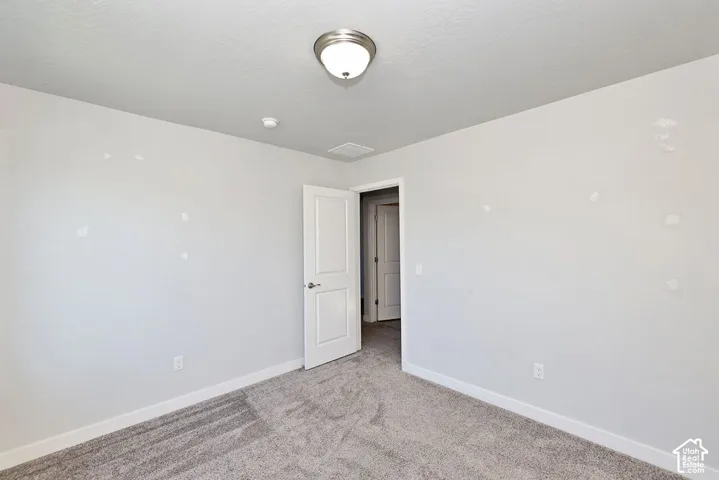 Interior room featuring neutral-toned carpeting, a brushed nickel flush-mount ceiling light fixture, and a solid-core interior door with a brushed nickel lever handle