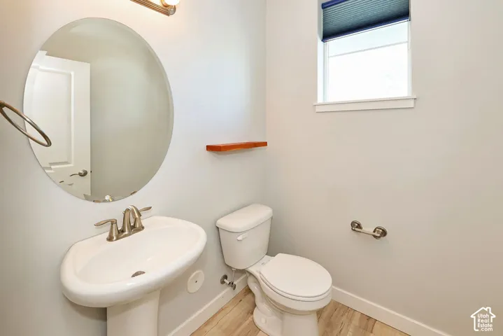 Pedestal sink with dual-handle faucet, oval mirror, wall-mounted natural wood shelf, and wood-finish flooring