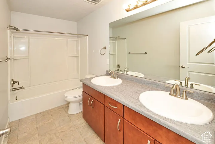 Bathroom featuring a dual-sink vanity with wood-finish cabinetry, a large full-width mirror, and a tub-shower combination with integrated shelving