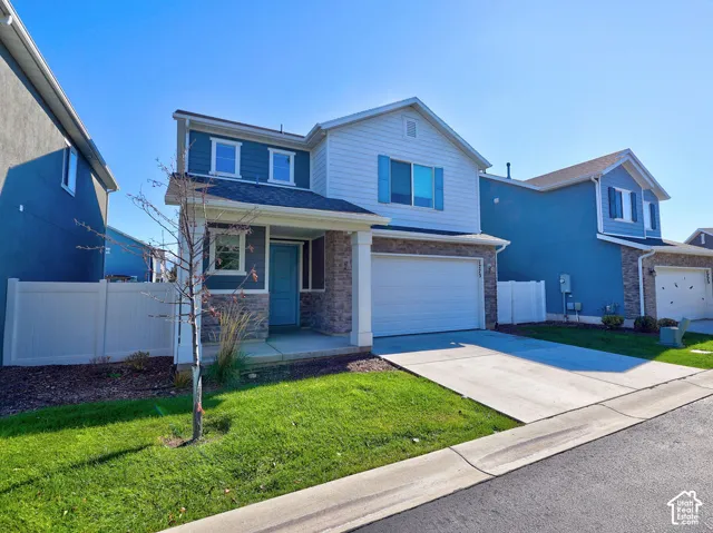 Two-story exterior featuring stone veneer accents, horizontal lap siding, a covered front entryway, attached two-car garage, and white vinyl perimeter fencing