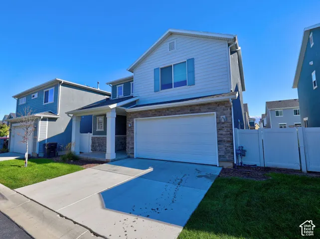 Two-story exterior featuring lap siding, stone veneer accents, a covered front porch with square columns, an attached two-car garage, and white vinyl privacy fencing