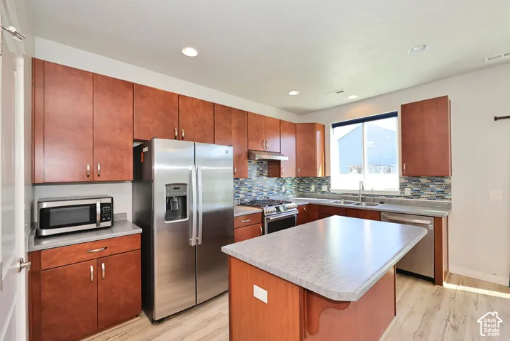 Kitchen featuring wood-finish cabinetry, a center island with a laminate countertop, stainless steel appliances, and multi-colored glass tile backsplash