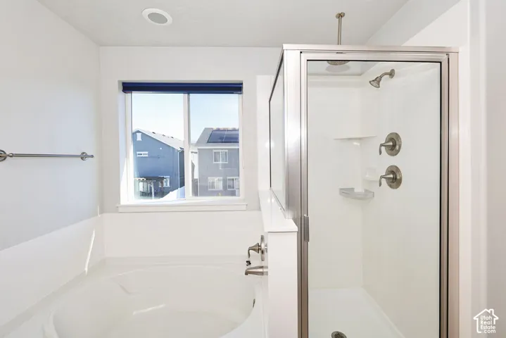 Soaking tub with a wall-mounted faucet, separate enclosed shower stall, recessed ceiling lighting, and a window with natural light