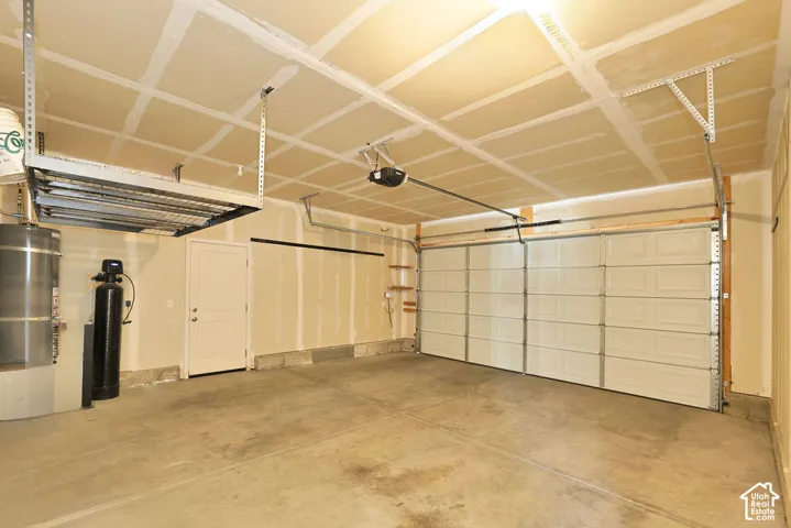 Attached garage featuring a concrete floor, multi-panel overhead door, suspended overhead storage rack, and water treatment system