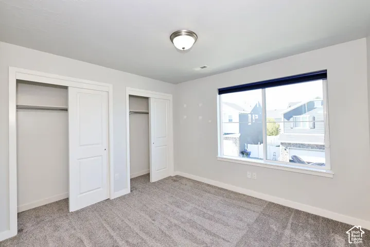 Room featuring neutral wall tones, wall-to-wall carpeting, dual closets with interior shelving, and a large window with a mounted shade