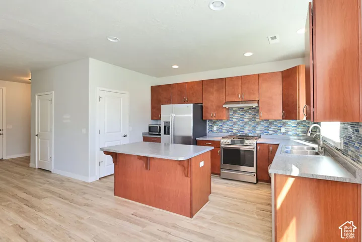 Kitchen featuring wood-finish cabinetry, a center island, stainless steel appliances, recessed lighting, and a multi-toned tile backsplash