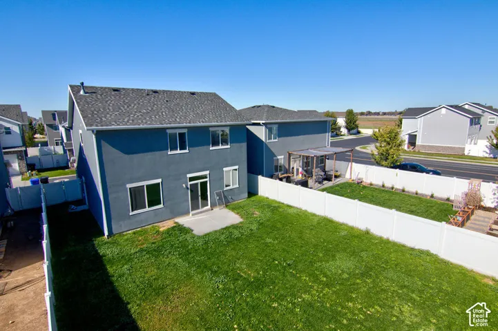 Two-story stucco exterior, backyard enclosed by white vinyl fencing, concrete patio, and asphalt shingle roof