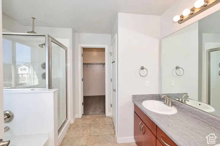 Bathroom featuring a vanity with stone-finish countertop and oval undermount sink, glass-enclosed shower, tile flooring, and oversized wall-mounted mirror