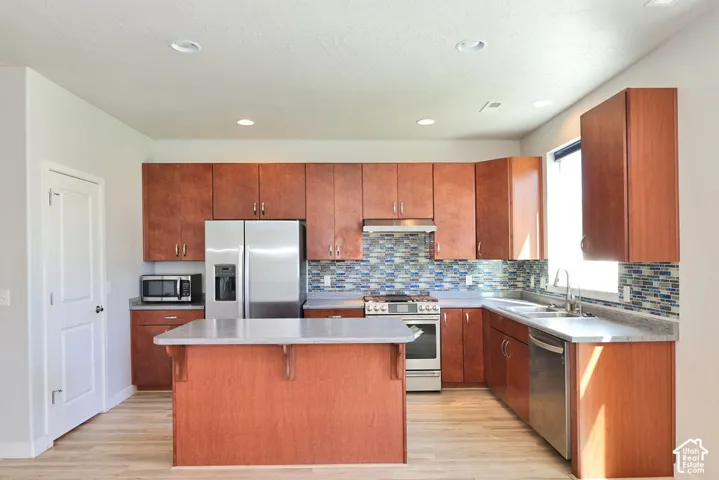 Kitchen featuring flat-panel wood cabinetry, a central island, multi-toned glass tile backsplash, stone-finish countertops, and stainless steel appliances