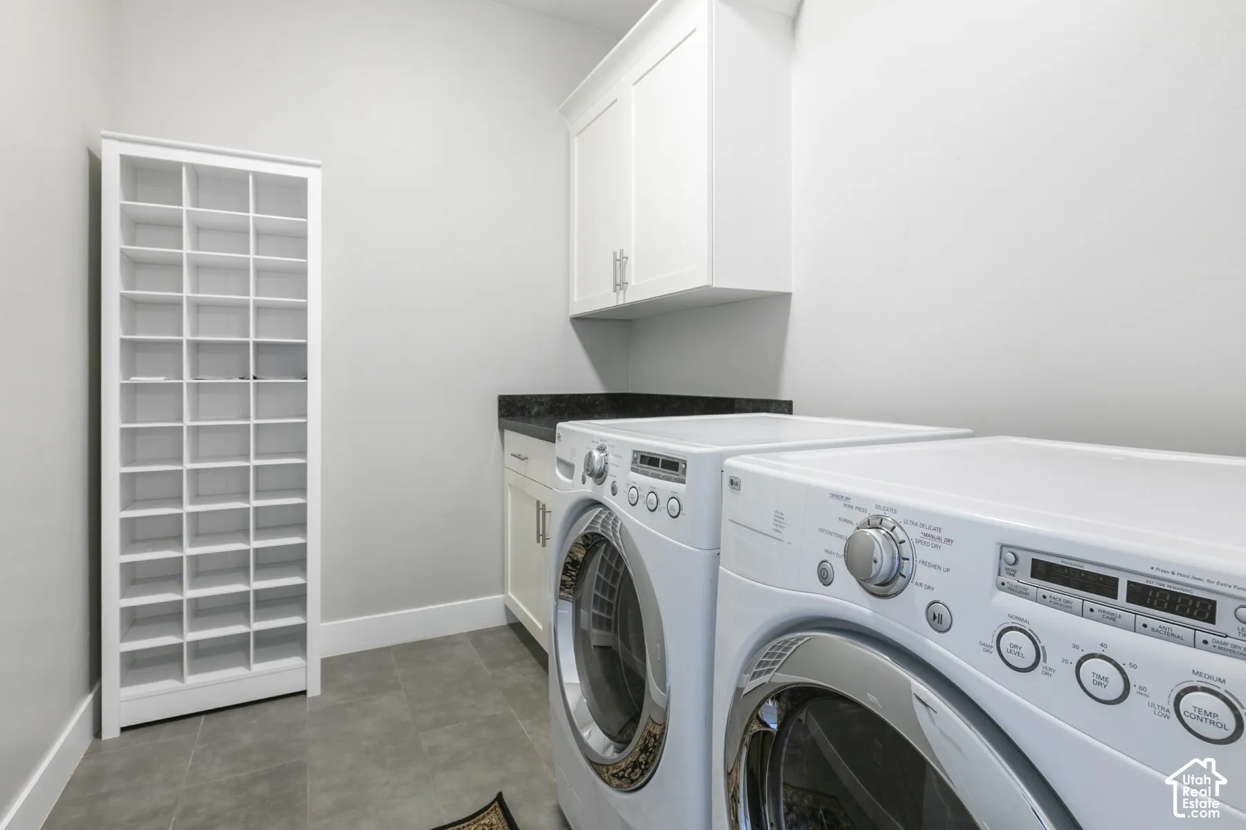 Laundry area featuring built-in floor-to-ceiling cubby shelving, upper and lower cabinetry, stone-finish countertops, and tile flooring