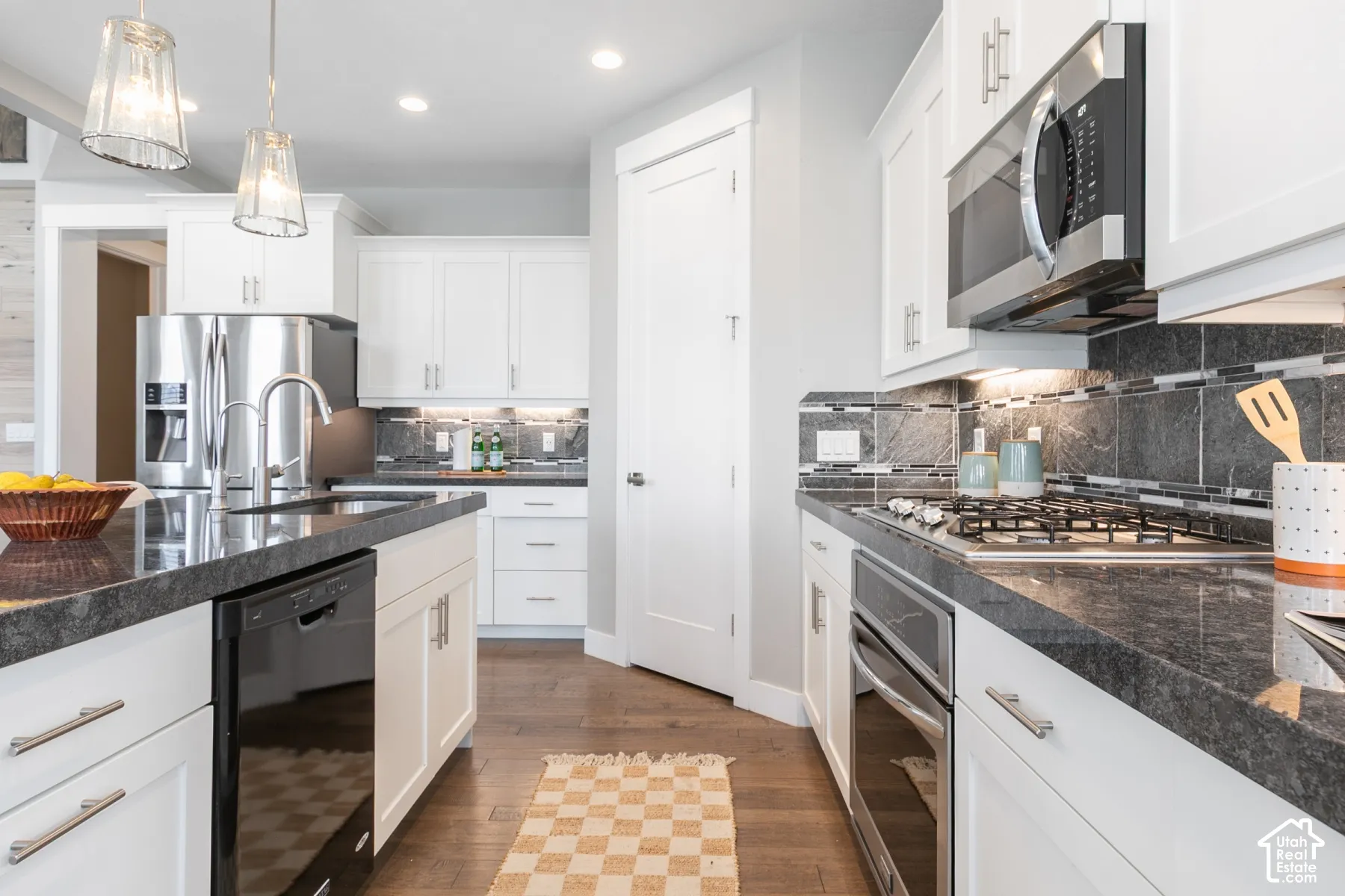 Kitchen featuring white cabinetry, dark stone countertops, stainless steel appliances, a multi-tonal linear tile backsplash, and wood-finish flooring
