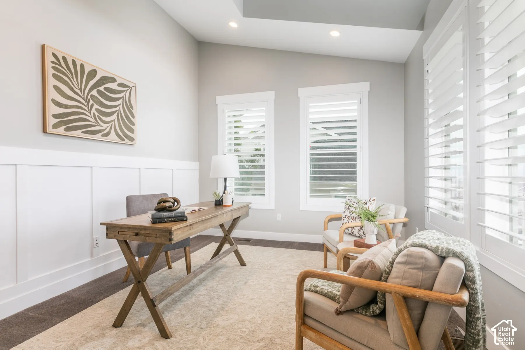 Room featuring a vaulted ceiling, white wainscoting, wood-finish flooring, and windows with plantation shutters