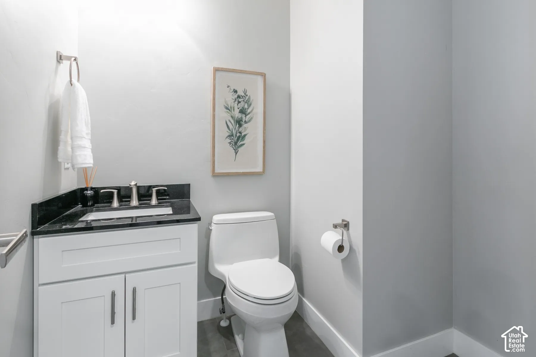 White shaker-style vanity with a dark stone countertop, integrated sink, polished metal widespread faucet, and large-format tile flooring