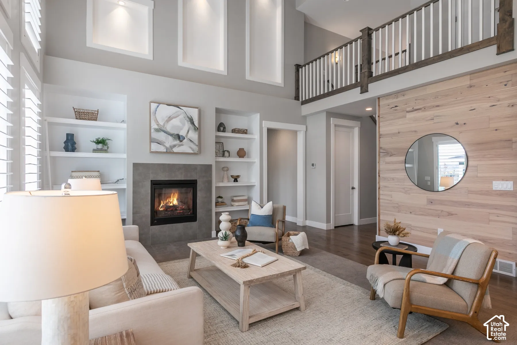 Double-height living area featuring a wood-plank accent wall, fireplace with stone surround, custom built-in shelving, and a wood-railing mezzanine