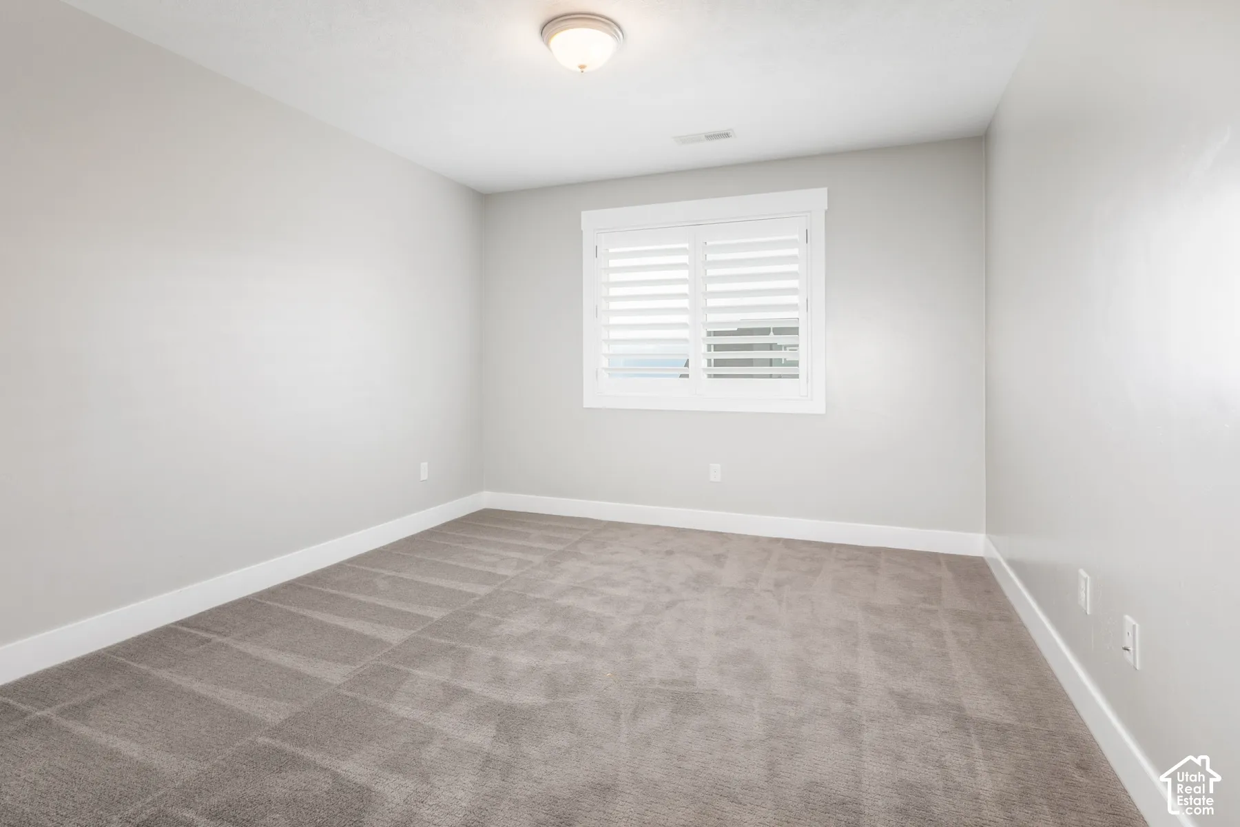 Neutral-toned bedroom featuring plush wall-to-wall carpeting, crisp white window trim, and plantation shutters