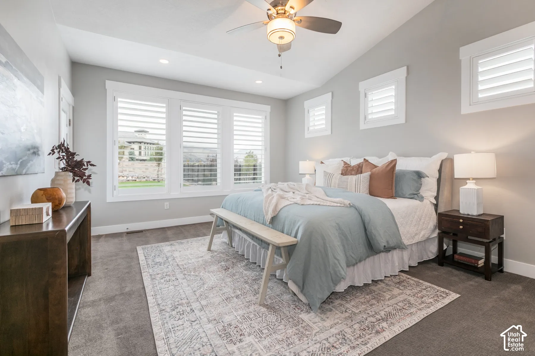 Vaulted ceiling featuring a central lighted ceiling fan, expansive triple-pane window array, and plantation shutters