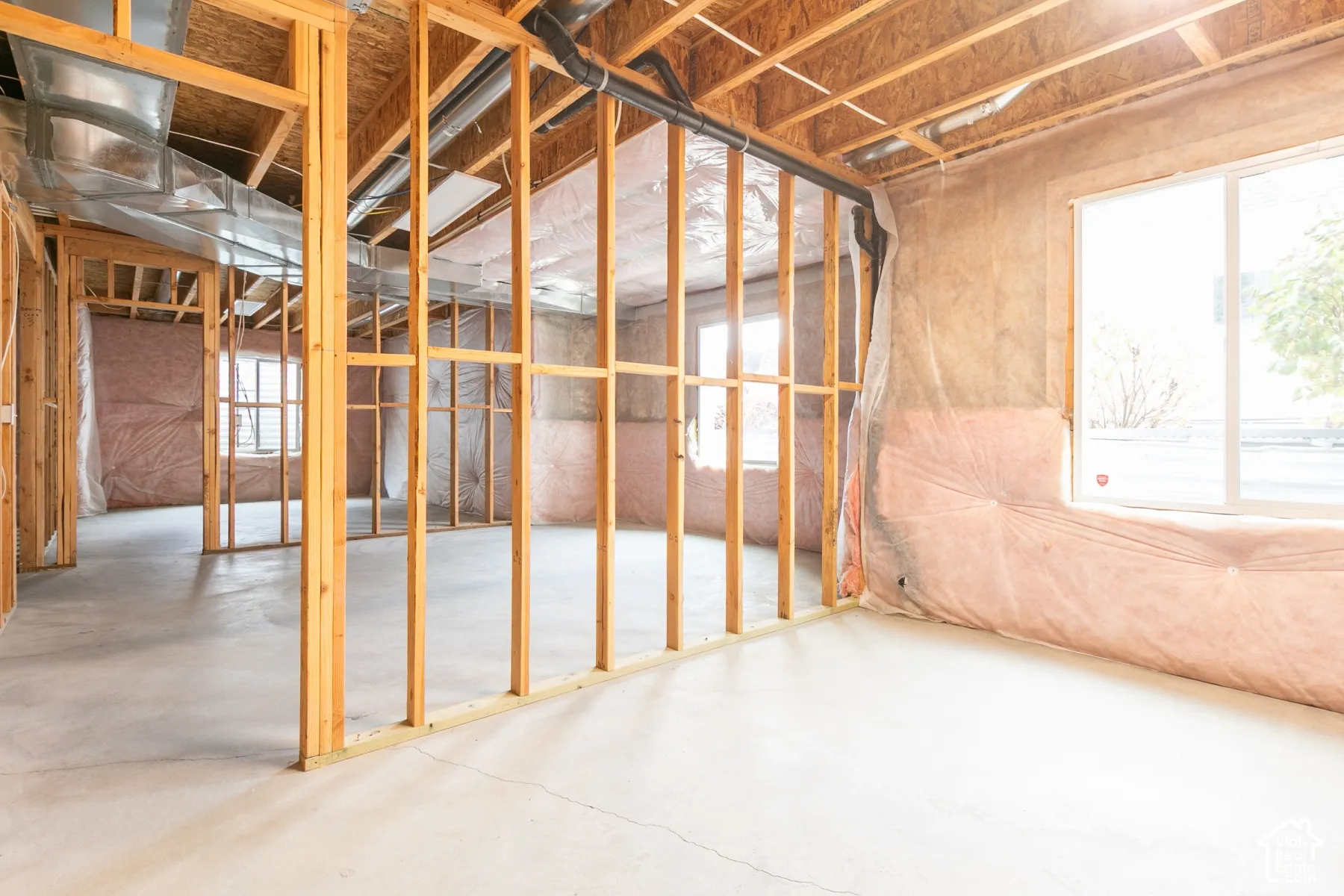 Unfinished interior space featuring exposed wood-stud framing, concrete flooring, installed wall insulation, and multi-pane windows