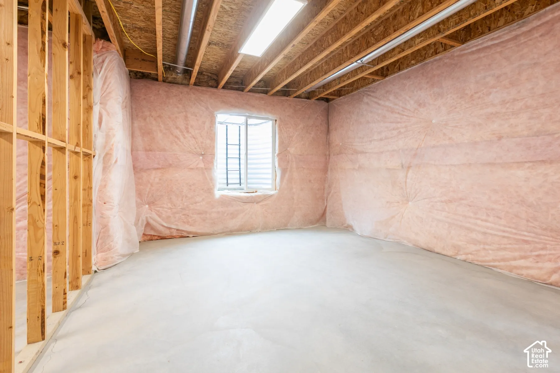Unfinished space featuring concrete flooring, exposed wooden ceiling joists, insulated walls, a window with a metal grate, and a rectangular light fixture