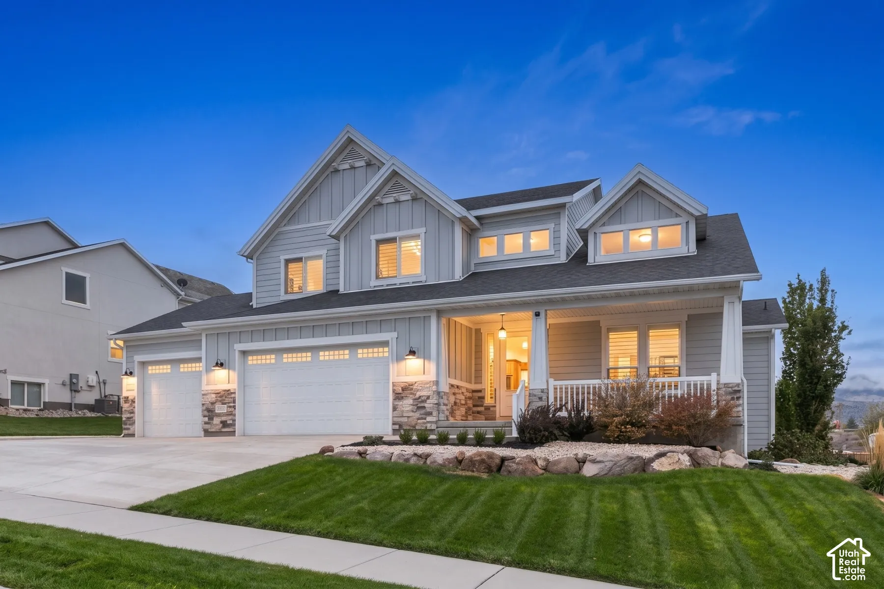 Two-story residence featuring vertical and horizontal siding, a stone veneer foundation, a three-car garage, and a covered front porch with a white railing