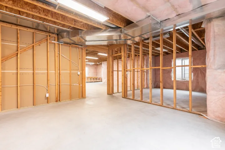 Unfinished lower level featuring exposed wood framing, concrete flooring, pink fiberglass insulation, and mounted linear lighting