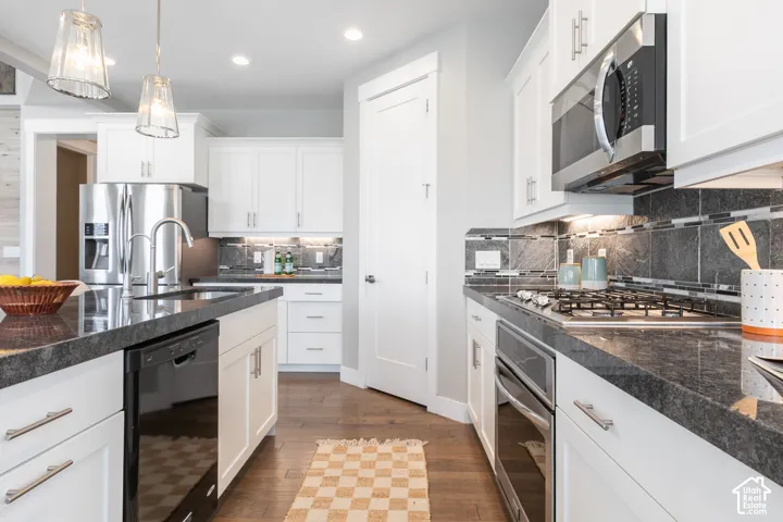 Kitchen featuring white cabinetry, dark stone countertops, stainless steel appliances, a multi-tonal linear tile backsplash, and wood-finish flooring