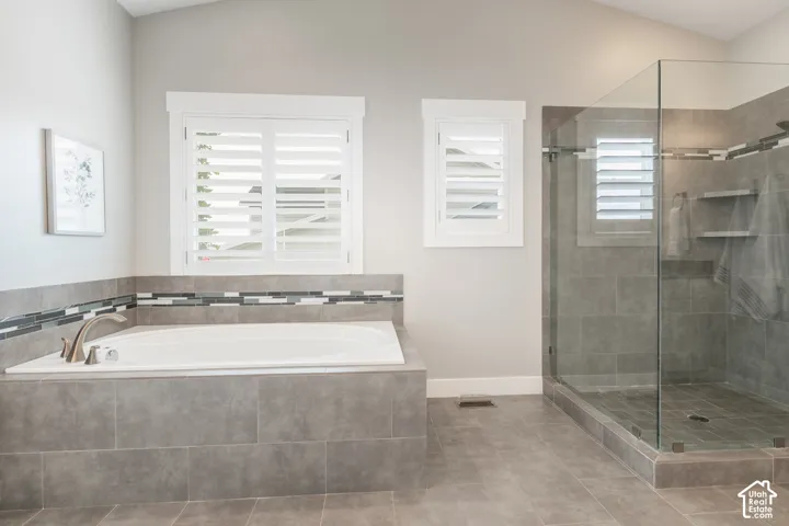 Soaking tub with tile surround, glass-enclosed walk-in shower, decorative mosaic tile accents, and plantation shutters