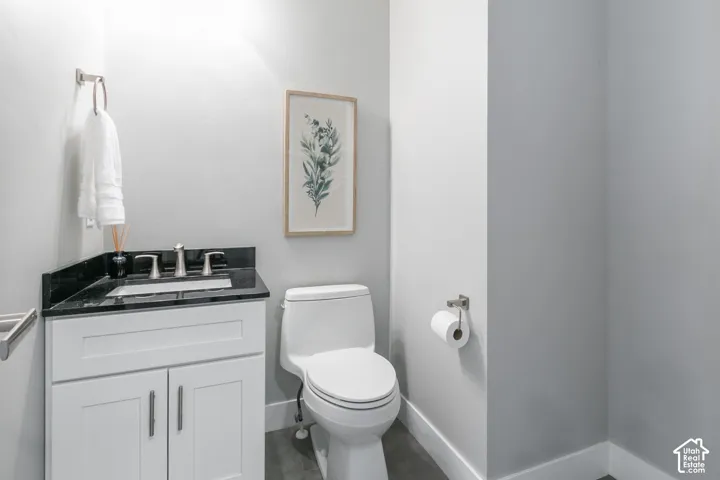 White shaker-style vanity with a dark stone countertop, integrated sink, polished metal widespread faucet, and large-format tile flooring