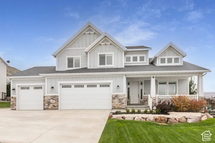 Multi-level exterior featuring vertical and horizontal siding, stone veneer accents, a covered front porch, and a three-car garage