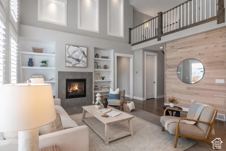 Double-height living area featuring a wood-plank accent wall, fireplace with stone surround, custom built-in shelving, and a wood-railing mezzanine