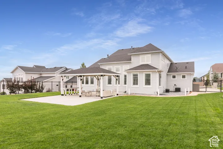 Expansive backyard featuring a manicured lawn, permanent covered pavilion, concrete patio, and perimeter metal fencing