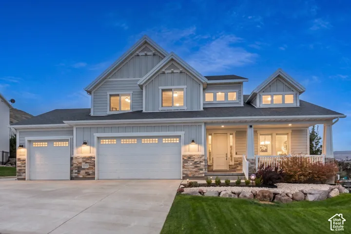 Multi-level residence featuring vertical siding, stone veneer accents, a three-car garage, and a covered front porch with a white balustrade