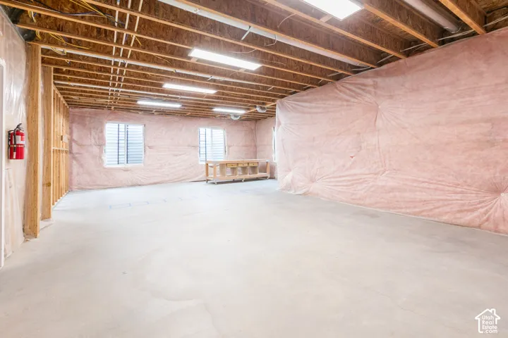 Unfinished space featuring exposed ceiling joists, concrete flooring, exterior-facing windows, batt insulation, and flush-mounted fluorescent lighting
