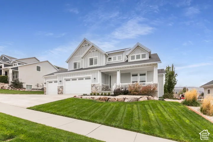 Two-story exterior featuring board-and-batten siding, stone veneer accents, an attached three-car garage, and a covered front porch with white railings