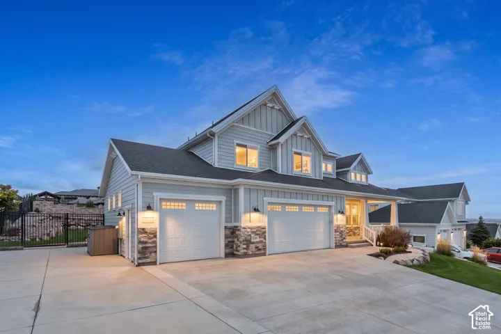 Multi-level exterior featuring horizontal lap siding, stone veneer accents, a three-car garage, and integrated wall-mounted exterior lighting