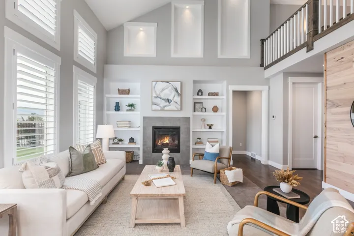 Vaulted ceilings with recessed alcove lighting, a floor-to-ceiling tiled fireplace, built-in shelving, wood-finish flooring, and a second-level landing with white railings
