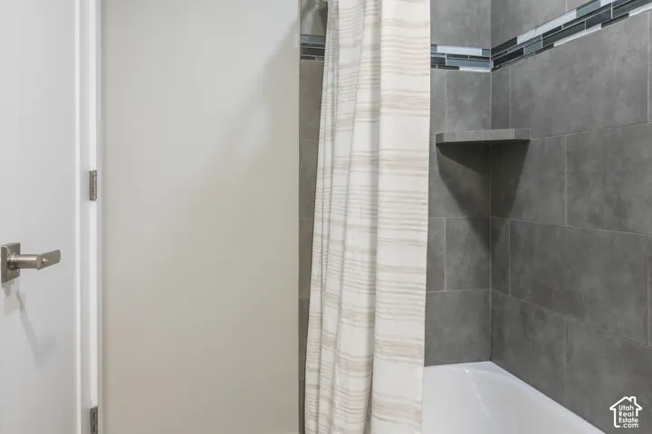 Bathtub surround featuring large-format dark grey tile, built-in corner shelving, and a glass and stone mosaic accent tile border