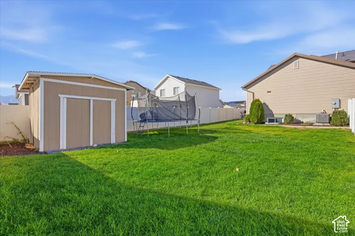 Rear yard featuring a manicured lawn, full-perimeter vinyl fencing, and a detached storage shed