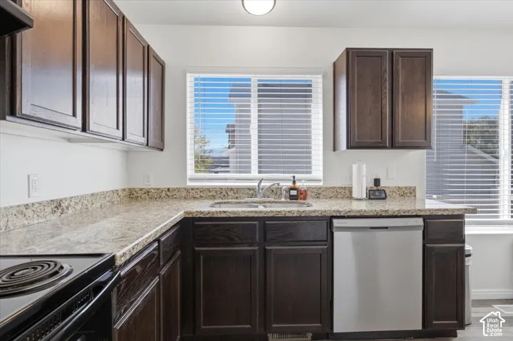 Kitchen featuring stained wood cabinetry, stone-surface countertops, dual-basin sink, and stainless steel dishwasher