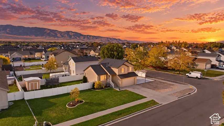 Two-story residence featuring a two-car garage, white vinyl fencing, and an expansive lawn set against a prominent mountain backdrop