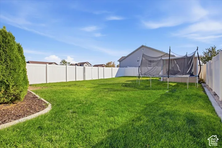 Backyard featuring a manicured lawn, white vinyl fencing, and a curved landscape border with mulch