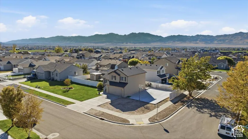 Corner lot featuring a concrete driveway, two-car garage, white vinyl fencing, and mountain backdrop