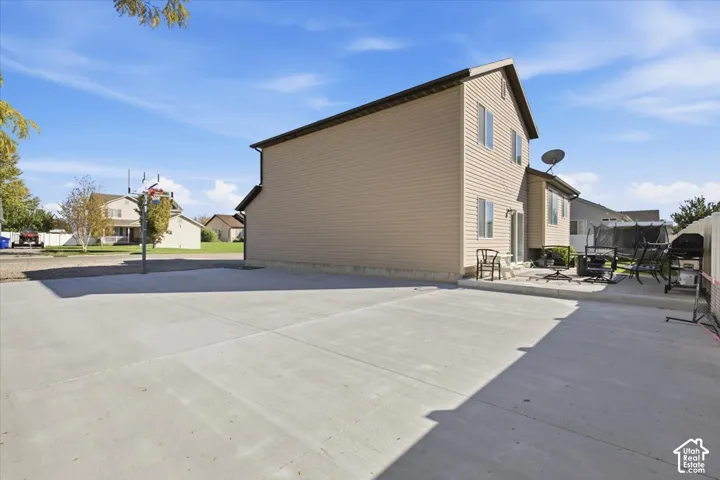 Two-story residence featuring light-toned horizontal siding, a spacious concrete parking area, and a concrete patio